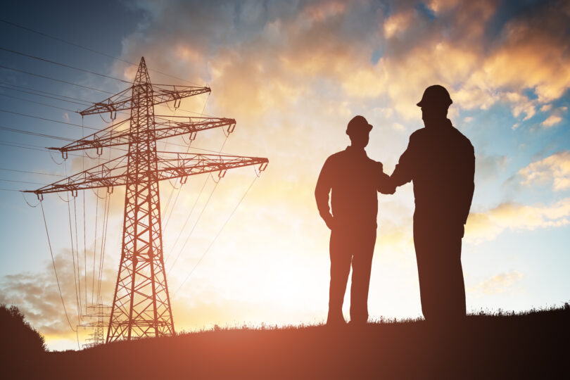 Silhouette,Of,Two,Engineers,Shaking,Hands,With,Electricity,Pylon,Against